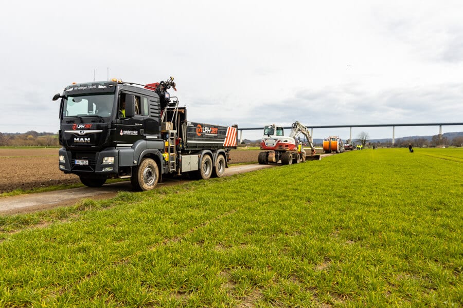 Panoramabild von den Arbeiten des Mülheimer GigaGlasfaserausbaus in der Saarner Ruhraue mit dem Layjet-Verfahren. Im Vordergrund eine LKW, dem ein Bagger folgt, der bereitet die Trasse vorbereitet, diesem folgt die Glasfaser-Verlegeinheit. 