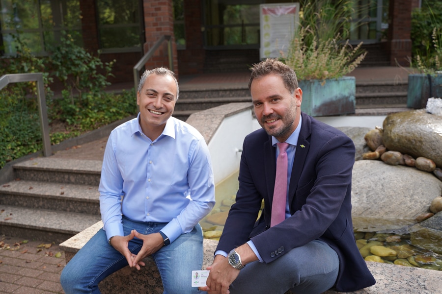 Zwei Männer, Tarek Moussa von der NFC21 GmbH links und Jan Hoffmann medl-Vertriebsleiter rechts mit der NFC-vCard in der Hand, sitzen an einem Brunnen vor dem medl-Gebäude