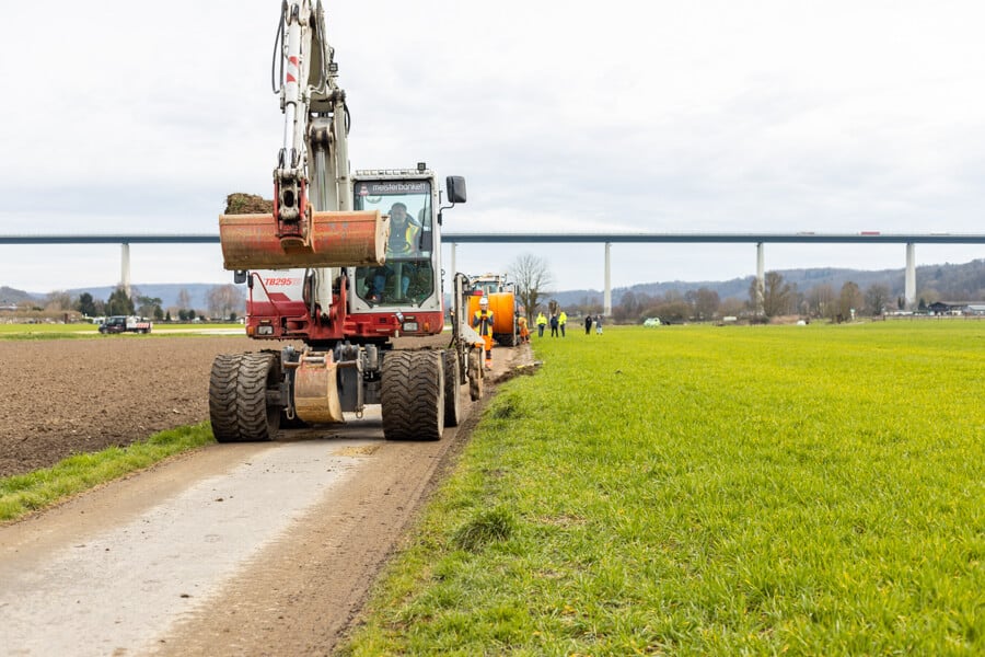 Ein Bagger beim Glasfaserausbau mit Layjet-Technologie bereitet die schmale Trasse im Randbereich einer Straße in der Saarner Ruhraue vor.  