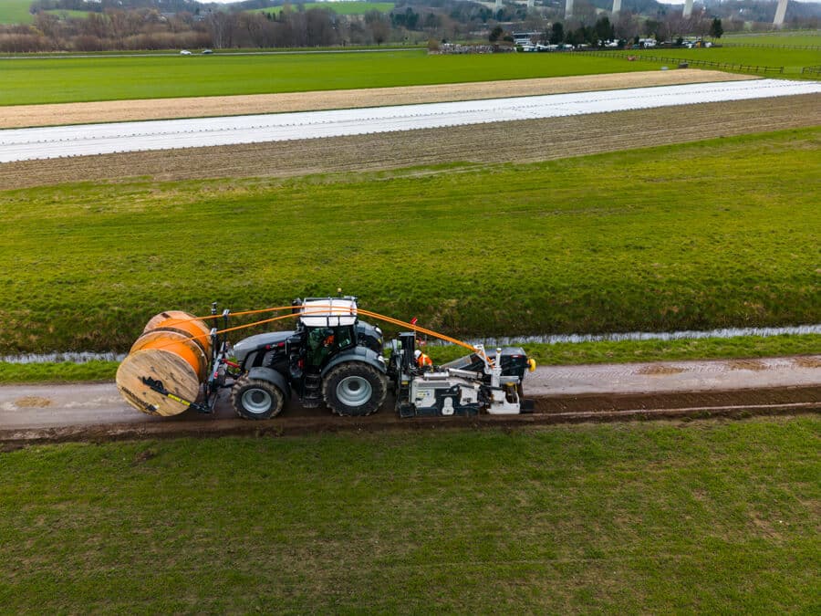 Luftaufnahme von der sog. Layjet-Verlegeeinheit, die neben der Asphaltkante eines Wegs in der Saarner Ruhraue einen Schlitzgraben fräst, Rohr und Warnband verlegt und den Boden gleichzeitig wieder verfüllt.