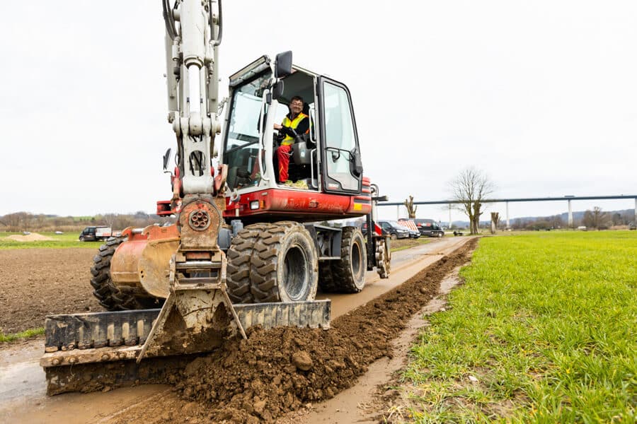 Bagger verdichtet und säubert die Trasse nach dem Glasfaserausbau mit Layjet-Technologie im Randbereich einer Straße in der Saarner Ruhraue.
