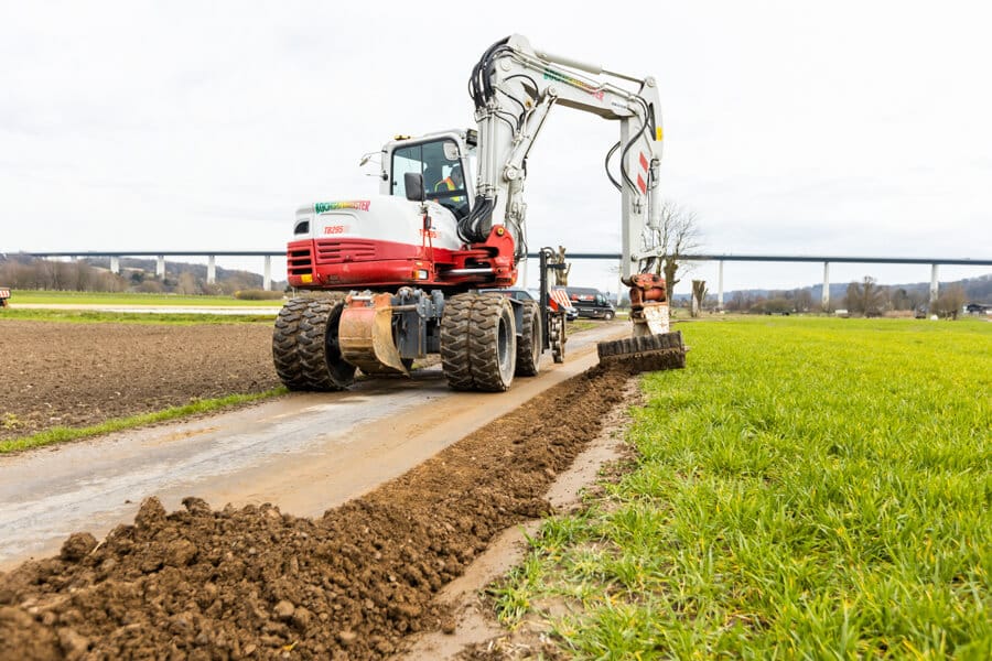 Bagger verdichtet und säubert ein zweites Mal die Trasse nach dem Glasfaserausbau mit Layjet-Technologie im Randbereich einer Straße in der Saarner Ruhraue.