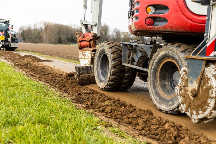 Bagger verdichtet und säubert zum wiederholten Mal die Trasse nach dem Glasfaserausbau mit Layjet-Technologie im Randbereich einer Straße in der Saarner Ruhraue.
