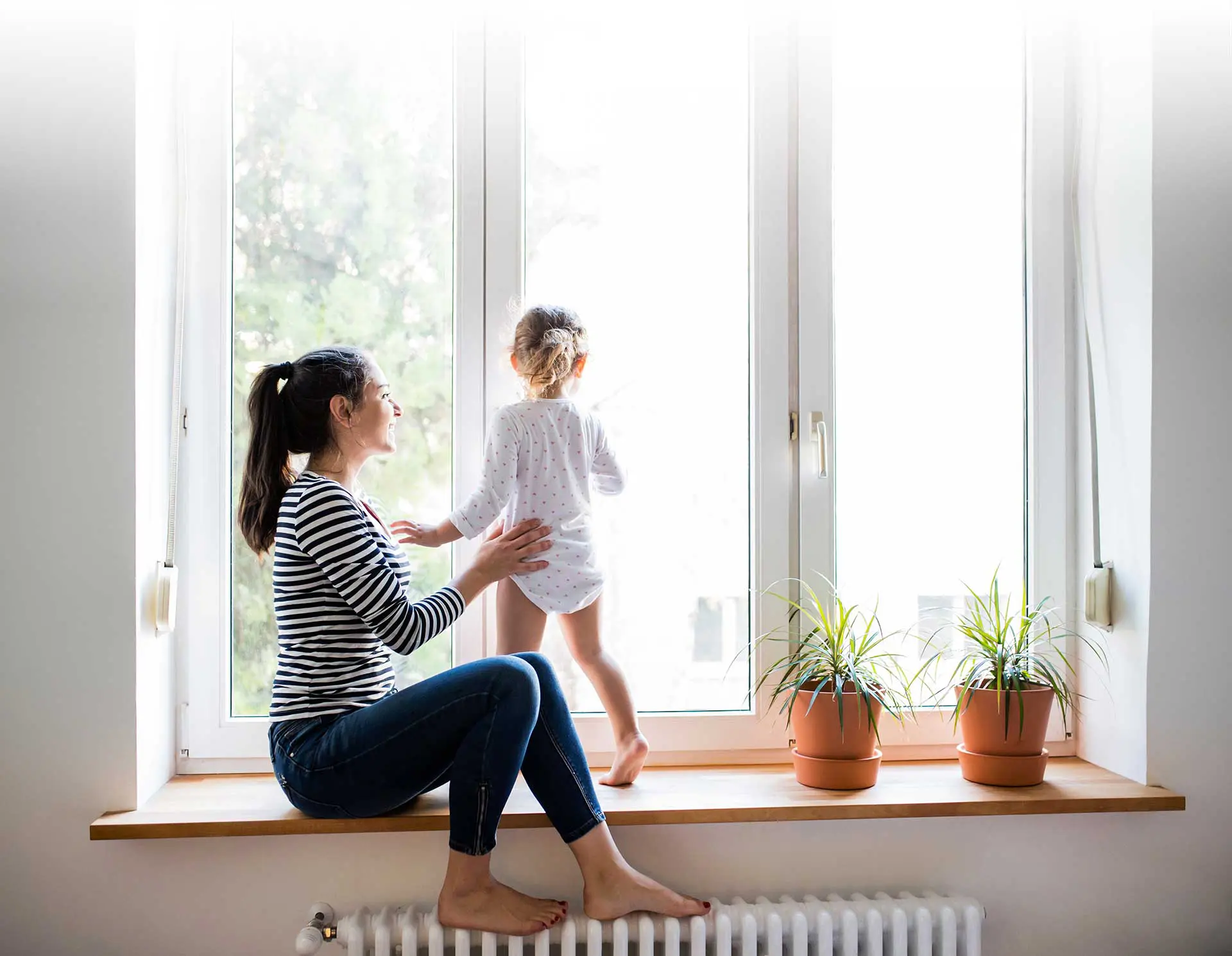 Mutter mit Kind sitzend auf Fensterbank und Heizung