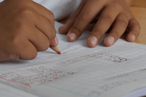 Großaufnahme von Kinderhänden mit einem Stift beim Lösen von Schulaufgaben