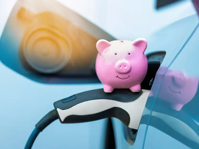 Rosa Sparschwein sitzt auf einem Ladestecker, der ein eAuto lädt – Symbol für faires und individuelles Abrechnen der Ladeleistung in Wohnungseigentümergemeinschaften.
