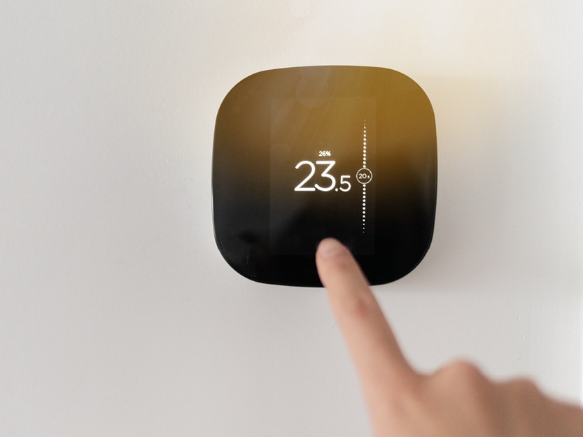 Finger stellt die Temperatur an einem digitalen Wandthermostat ein.