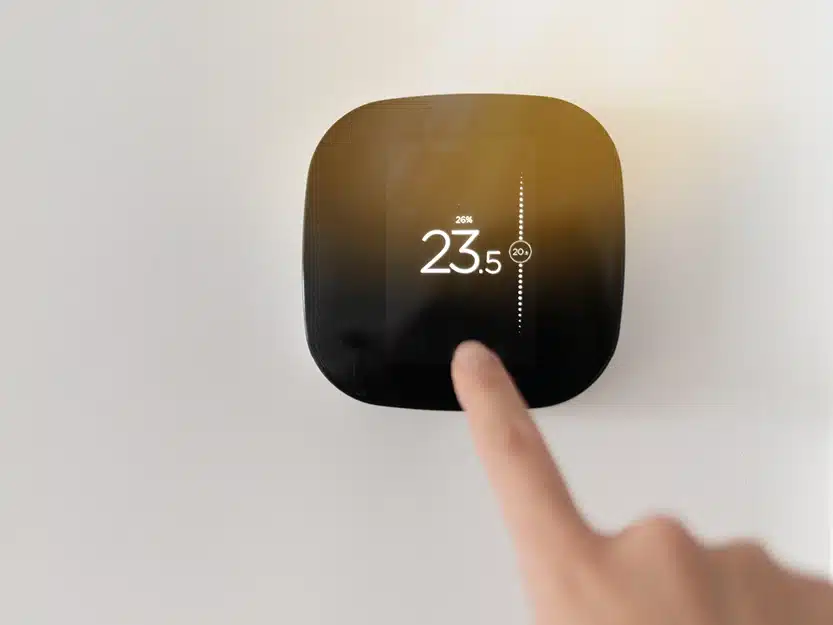 Finger stellt die Temperatur an einem digitalen Wandthermostat ein.