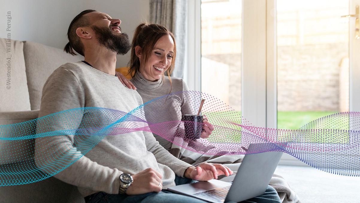 Lachendes Paar am Laptop mit gigaverliebt-Logo und grafischen Wellen für stabiles Glasfaser-Internet.