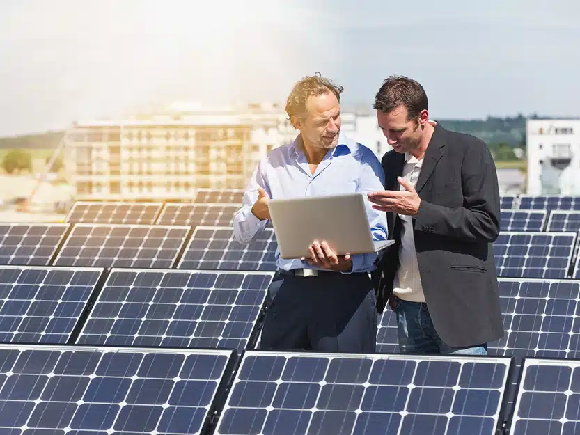 Zwei Männer mit Laptop inmitten einer Solaranlage symbolisieren die aktive Gestaltung der Energiewende durch medl.