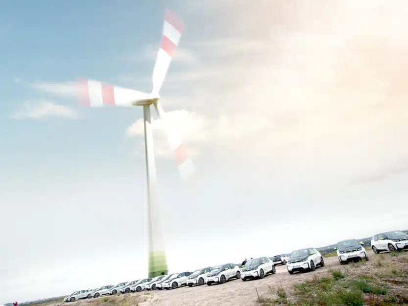 medl Windrad in Mülheim mit davor parkender eAuto-Flotte, symbolisiert lokale Grünstrom-Erzeugung.