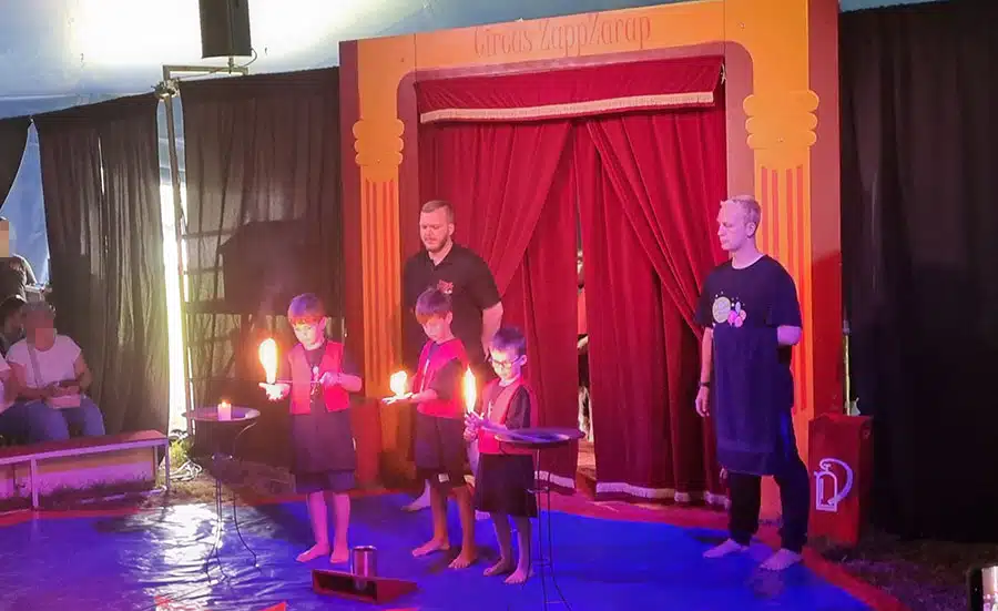 Kinder und Betreuer beim medl-Mitmach-Zirkus Eine Gruppe fröhlicher Kinder und Zirkusbetreuer steht dicht beisammen in der Manege des medl-Mitmach-Zirkus'.