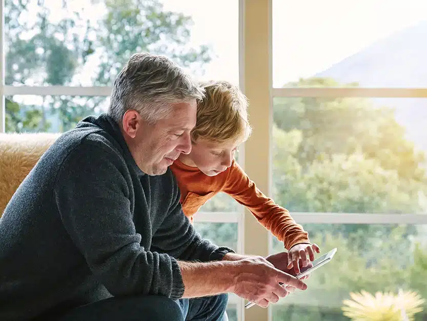 Großvater und Enkel bedienen gemeinsam ein Tablet im Wohnzimmer – Symbolbild für den kinderleichten Wechsel zu medl Ökogas.