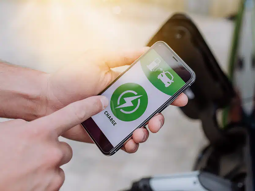 Großaufnahme von einem Handy in einer Hand mit geöffneter Lade-App, die den Ladevorgang anzeigt, auf die eine andere Hand zeigt – Symbol für sicheres Laden zu Hause.