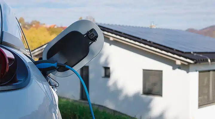 Nahaufnahme eines E-Autos beim Laden vor einem Einfamilienhaus mit Photovoltaikanlage auf dem Dach – ideal für das medl Sonnenstrom-Rundum-Paket.